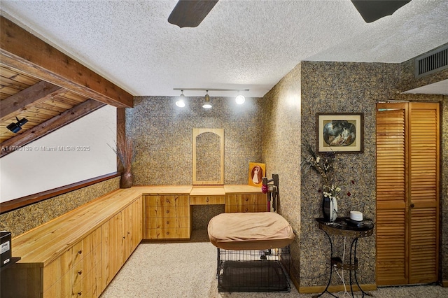 sitting room with a textured ceiling, built in desk, visible vents, and wallpapered walls