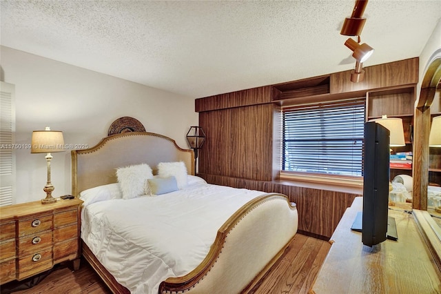 bedroom featuring wooden walls, a textured ceiling, and wood finished floors