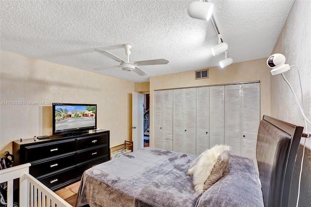 bedroom with a closet, rail lighting, visible vents, a ceiling fan, and a textured ceiling