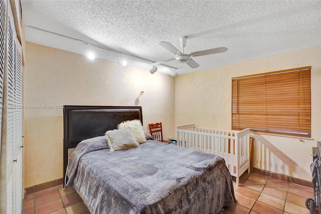 bedroom with a textured ceiling, light tile patterned floors, a ceiling fan, and baseboards