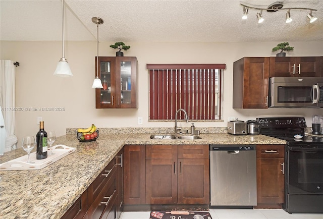 kitchen with light stone counters, glass insert cabinets, hanging light fixtures, stainless steel appliances, and a sink