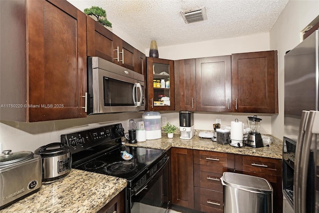 kitchen featuring stainless steel appliances, glass insert cabinets, visible vents, and light stone countertops