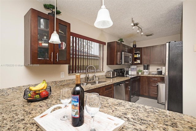 kitchen featuring light stone counters, pendant lighting, appliances with stainless steel finishes, glass insert cabinets, and a sink