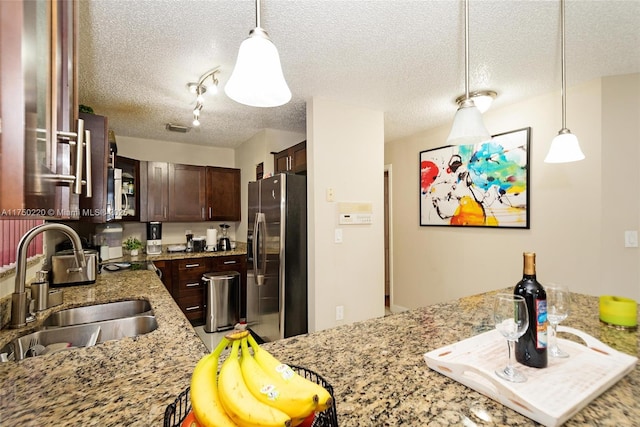 kitchen featuring stainless steel refrigerator with ice dispenser, hanging light fixtures, a sink, dark brown cabinets, and light stone countertops