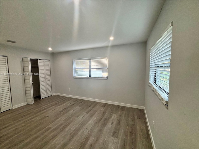 unfurnished bedroom with multiple closets, visible vents, baseboards, and wood finished floors