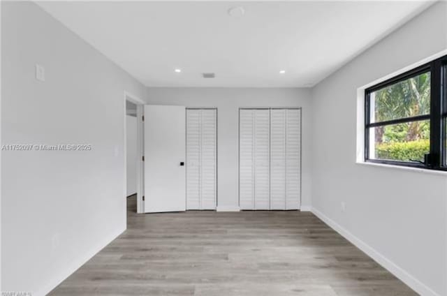 unfurnished bedroom with light wood-style flooring, baseboards, multiple closets, and recessed lighting