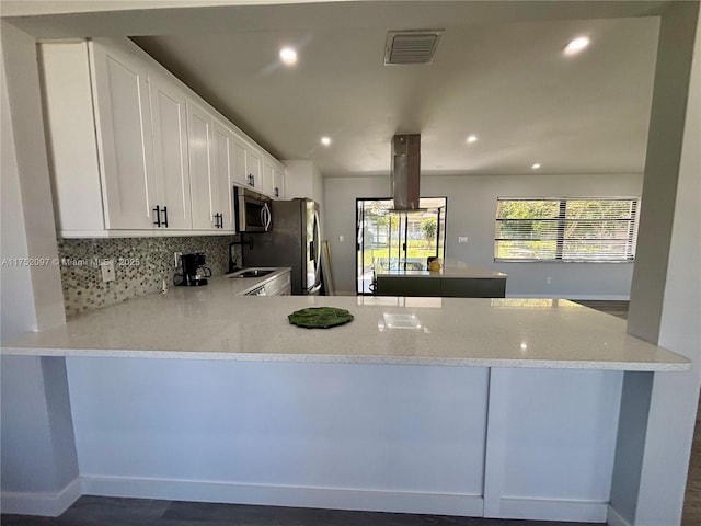 kitchen with visible vents, decorative backsplash, a peninsula, stainless steel appliances, and a sink