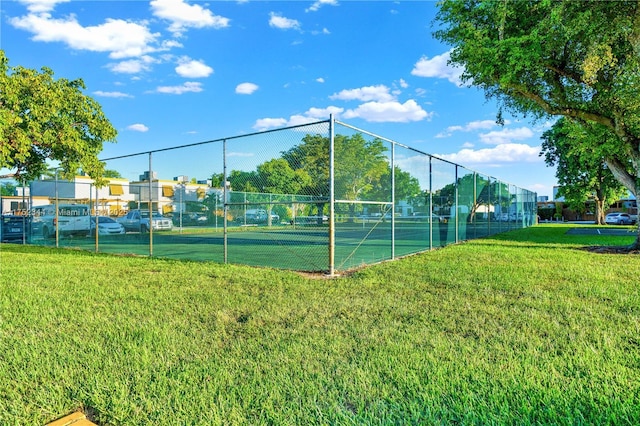 view of tennis court with fence and a yard