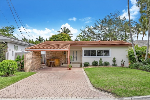 ranch-style house featuring a tile roof, brick siding, a front lawn, and stucco siding