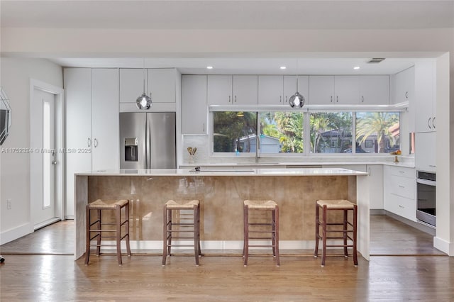 kitchen featuring a breakfast bar, a center island, light countertops, appliances with stainless steel finishes, and white cabinetry