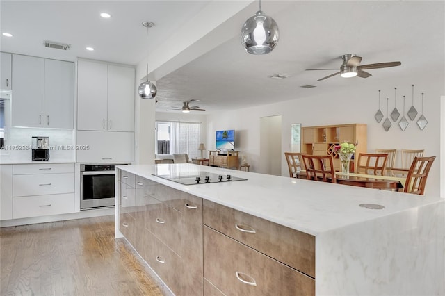 kitchen with oven, decorative light fixtures, black electric cooktop, light countertops, and white cabinetry