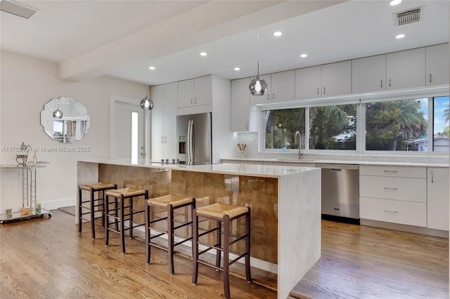 kitchen featuring stainless steel appliances, a kitchen island, visible vents, white cabinetry, and light countertops