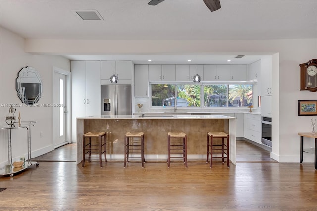 kitchen with a breakfast bar area, a kitchen island, white cabinets, light countertops, and appliances with stainless steel finishes