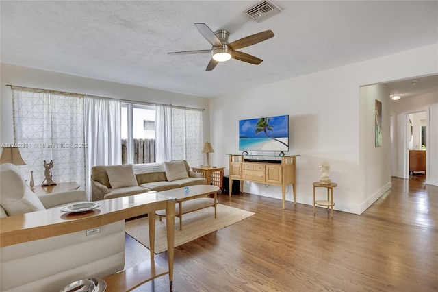 living room featuring visible vents, ceiling fan, baseboards, and wood finished floors