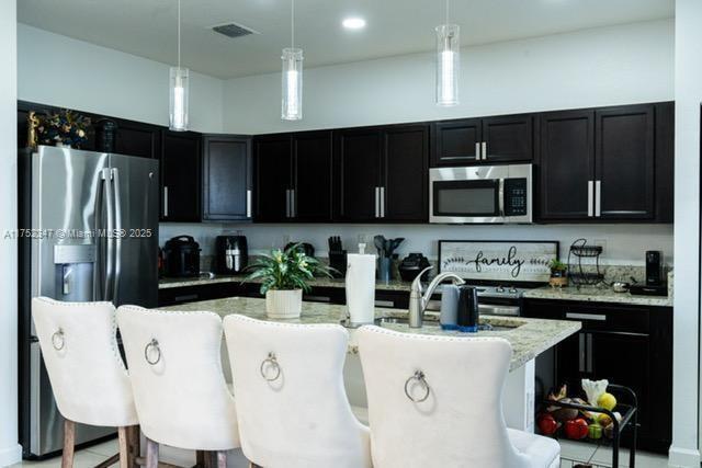 kitchen with appliances with stainless steel finishes, dark cabinets, visible vents, and decorative light fixtures