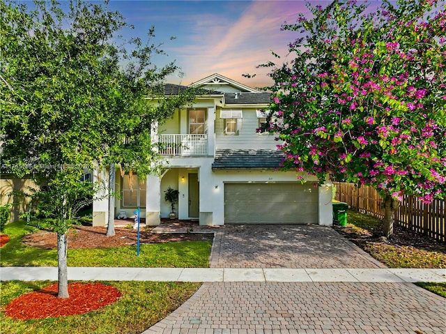 view of front of property with a balcony, a garage, fence, decorative driveway, and stucco siding