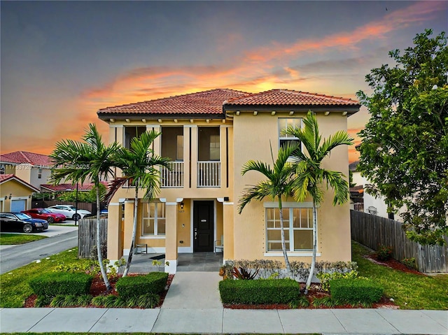 mediterranean / spanish-style home featuring a tile roof, fence, a balcony, and stucco siding