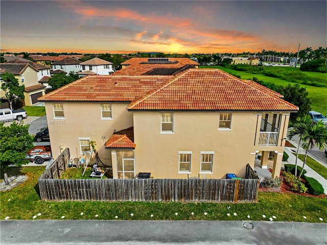 back of property at dusk with fence private yard, a tile roof, and stucco siding