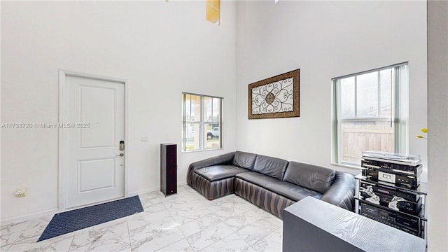 living area featuring a towering ceiling, marble finish floor, and baseboards