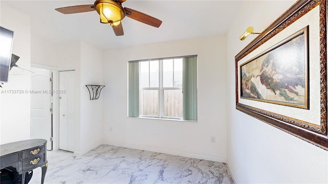 empty room featuring marble finish floor, ceiling fan, and baseboards