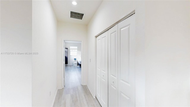 hall with baseboards, visible vents, and light wood finished floors