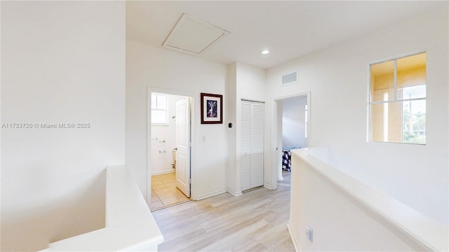 hall featuring light wood-type flooring, baseboards, visible vents, and a wealth of natural light