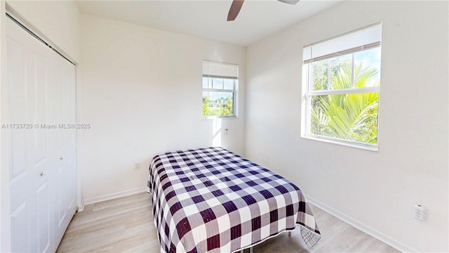 bedroom featuring a ceiling fan, a closet, light wood-style flooring, and baseboards