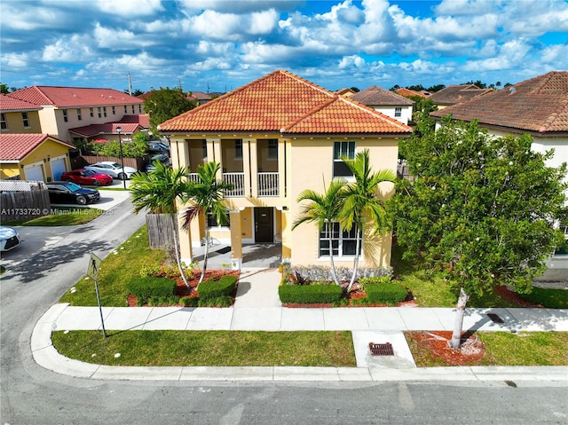 mediterranean / spanish house with a balcony, a tile roof, a residential view, and stucco siding