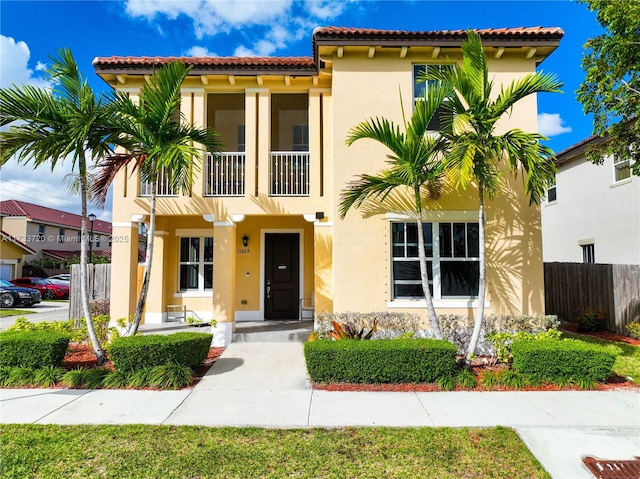 mediterranean / spanish-style home with fence, a tiled roof, and stucco siding