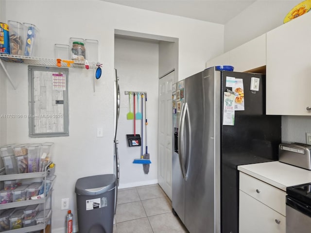 kitchen featuring light tile patterned floors, stainless steel fridge, range, light countertops, and white cabinetry