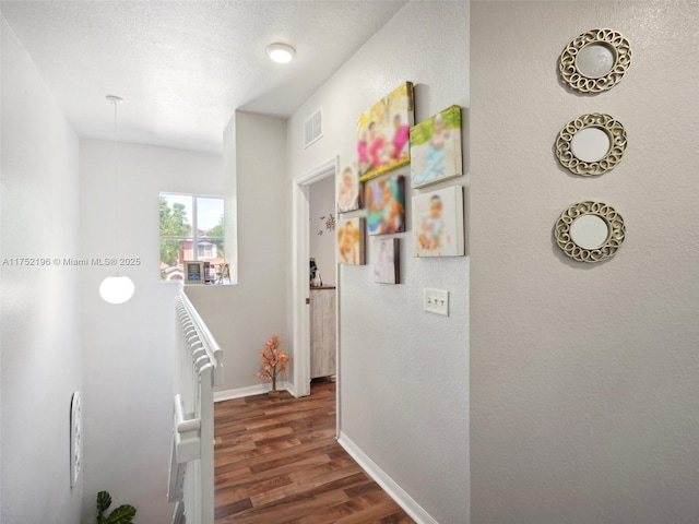 hall with visible vents, a textured wall, dark wood-type flooring, a textured ceiling, and baseboards