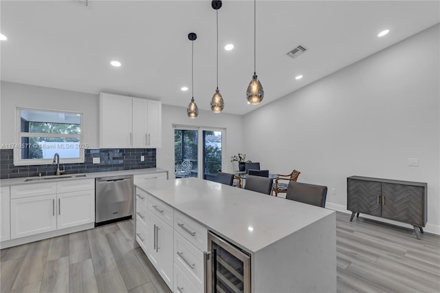 kitchen featuring beverage cooler, white cabinets, a sink, and stainless steel dishwasher