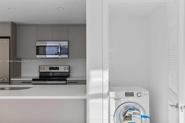 kitchen with light countertops, gray cabinetry, appliances with stainless steel finishes, a sink, and washer / dryer