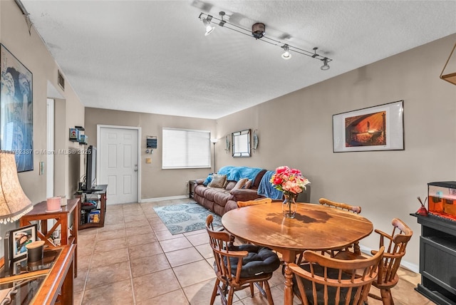 dining area featuring a textured ceiling, light tile patterned floors, visible vents, baseboards, and rail lighting