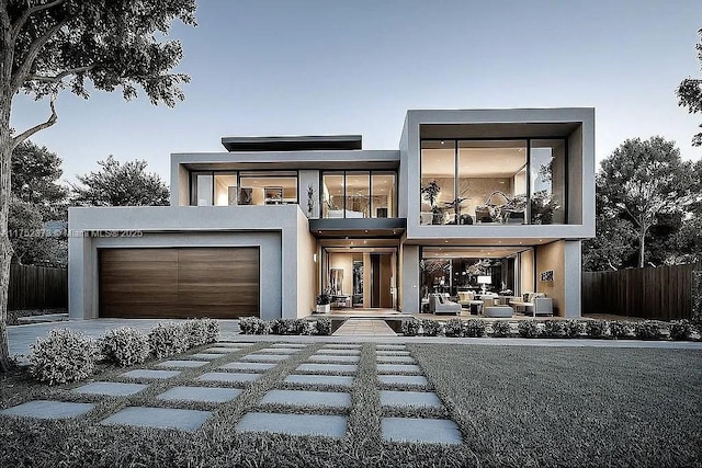 contemporary home featuring a garage, fence, a balcony, and stucco siding