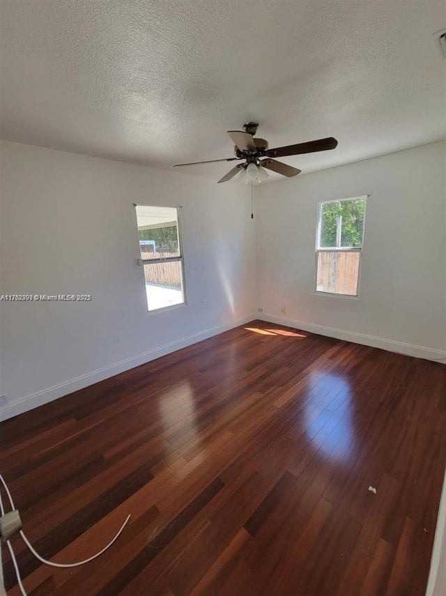 empty room with dark wood-style floors, plenty of natural light, and baseboards