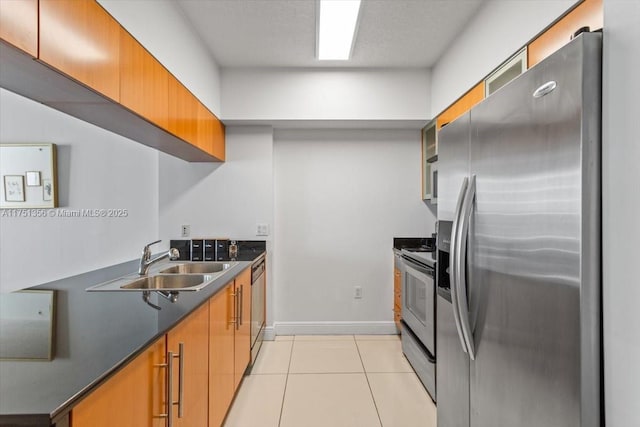 kitchen with appliances with stainless steel finishes, brown cabinetry, a sink, and light tile patterned floors