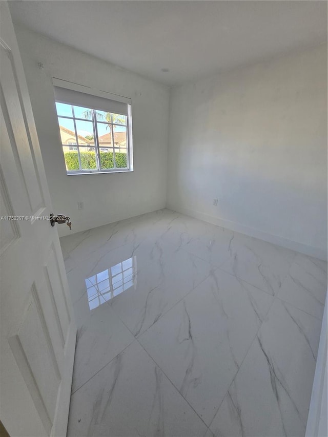 empty room featuring marble finish floor and baseboards