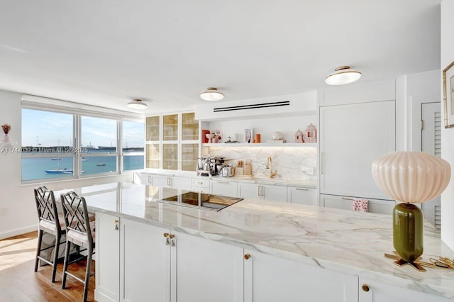 kitchen featuring light wood-style flooring, light stone countertops, black electric stovetop, white cabinetry, and open shelves