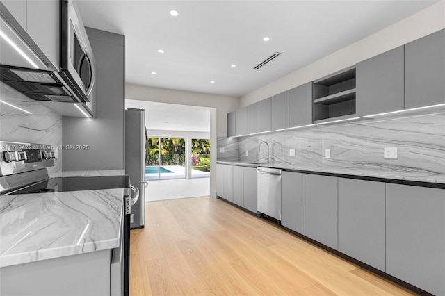 kitchen with visible vents, modern cabinets, appliances with stainless steel finishes, light stone counters, and gray cabinets