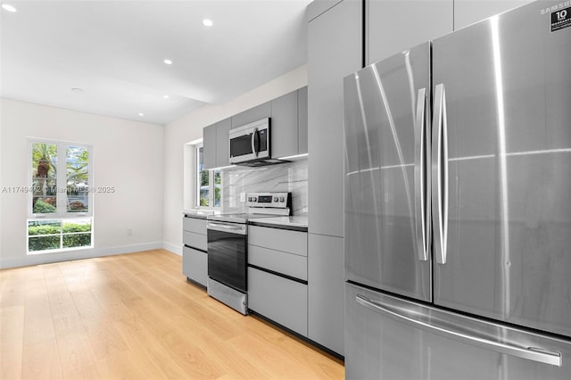 kitchen with light wood-style flooring, gray cabinetry, baseboards, appliances with stainless steel finishes, and tasteful backsplash