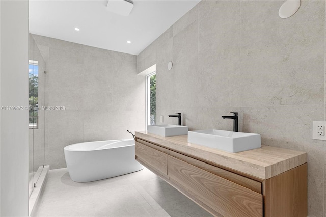 bathroom with double vanity, tile walls, a sink, and recessed lighting