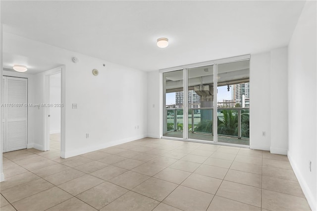 empty room with expansive windows, light tile patterned floors, and baseboards