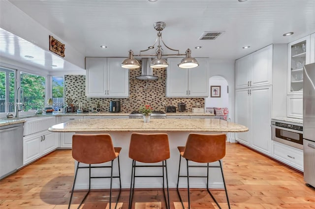 kitchen featuring visible vents, white cabinets, light wood-style floors, appliances with stainless steel finishes, and wall chimney range hood