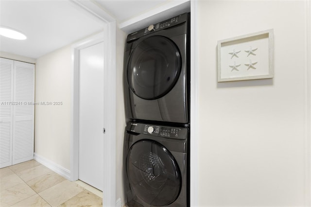 clothes washing area with marble finish floor, laundry area, stacked washing maching and dryer, and baseboards