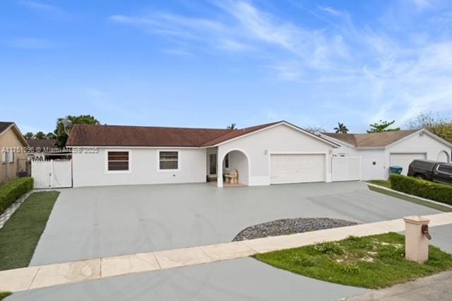 ranch-style house with concrete driveway, stucco siding, a gate, an attached garage, and fence