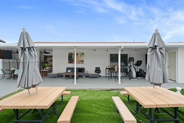 rear view of property with an outdoor living space, a patio, a lawn, and stucco siding