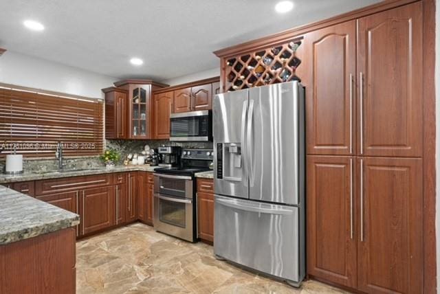 kitchen featuring glass insert cabinets, a sink, recessed lighting, stainless steel appliances, and light stone counters