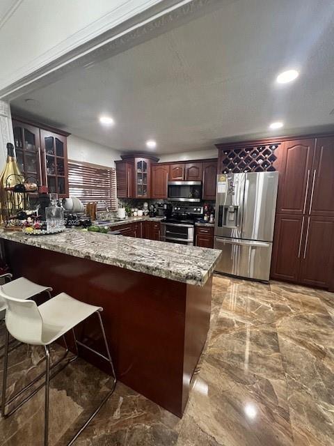 kitchen with stainless steel appliances, marble finish floor, glass insert cabinets, and a peninsula