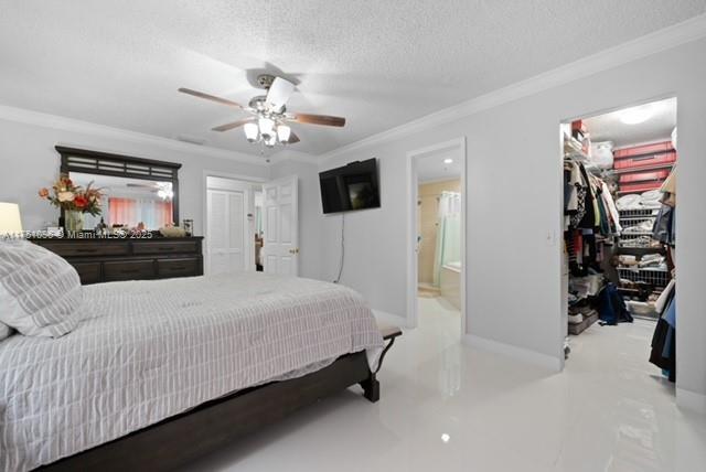 bedroom featuring baseboards, ornamental molding, a textured ceiling, a walk in closet, and ensuite bath